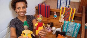 Janine Rodrigues com suas bonecas Abayomi, ao lado, o livro Bonecas Azuis, de sua própria autoria